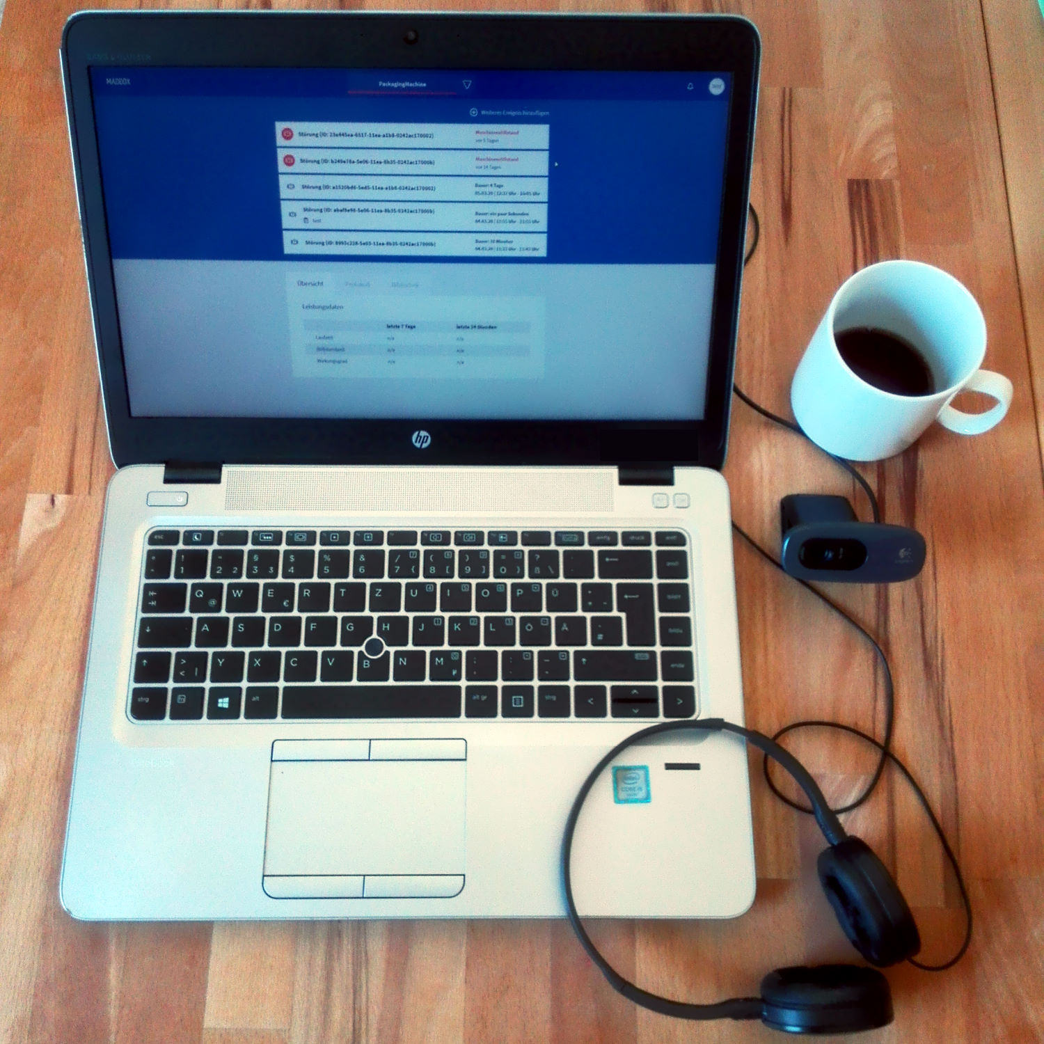 Homeoffice-Ausstattung während der Covid-19-Pandemie mit Laptop, Webcam, Headset und Kaffeetasse – ermöglicht ortsunabhängige Softwareentwicklung.