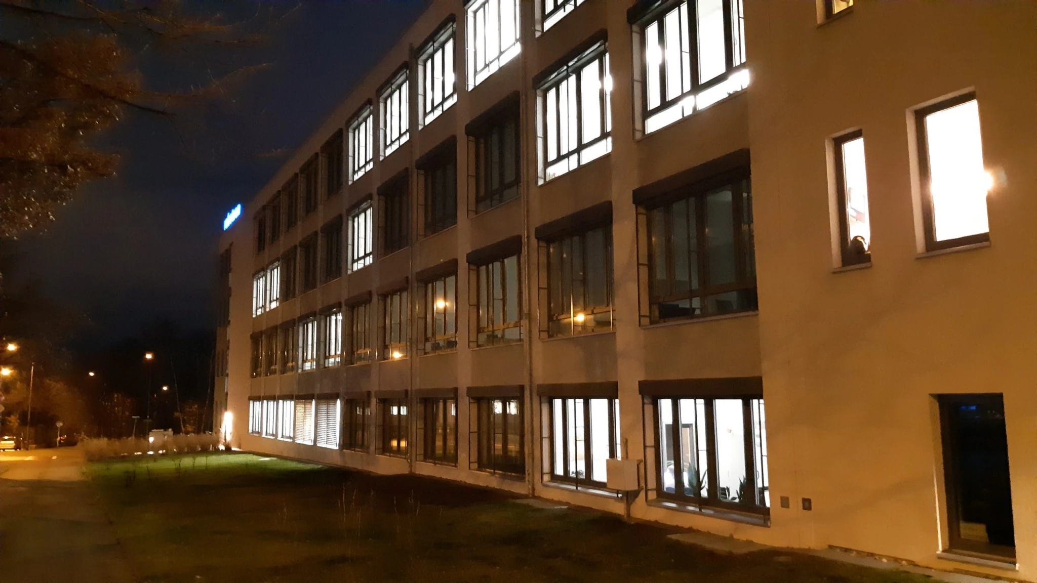 Gebäude mit beleuchteten Fenstern, rechts mit Eingangstür.