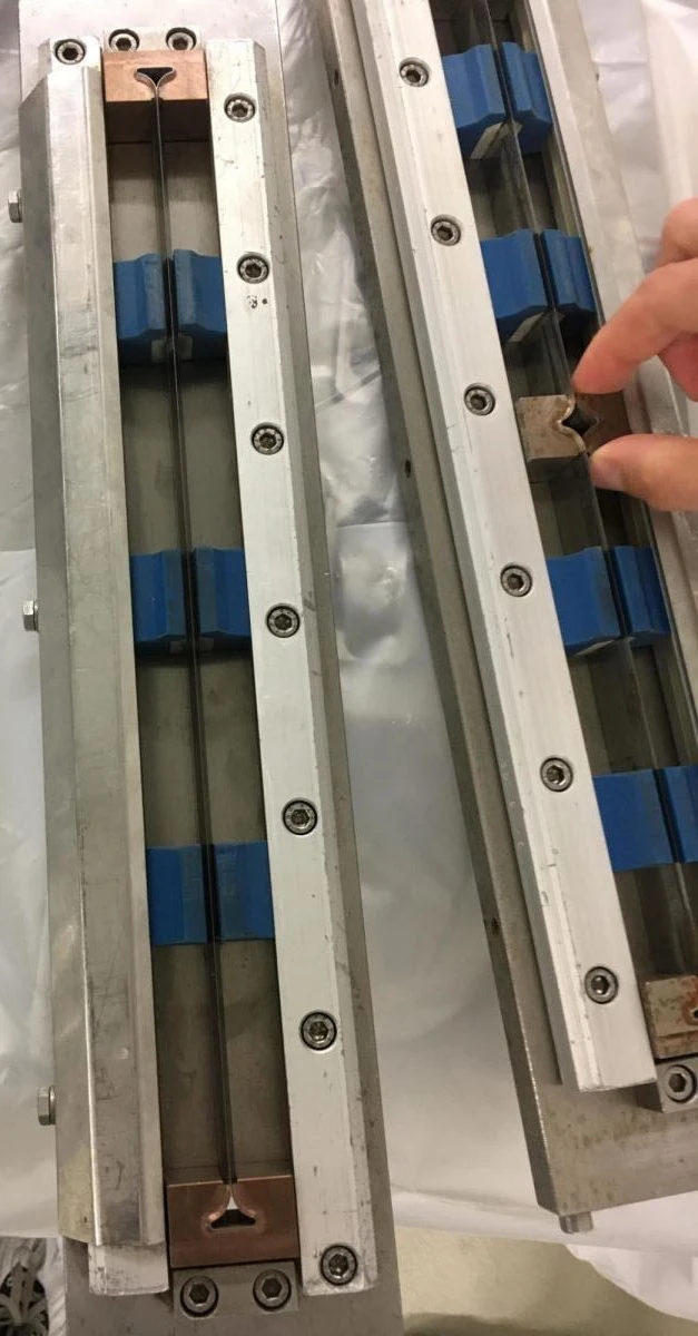 Maschinenteil mit blau markierten Elementen und einer Hand – Beispiel für uneinheitliche Begriffsnutzung.