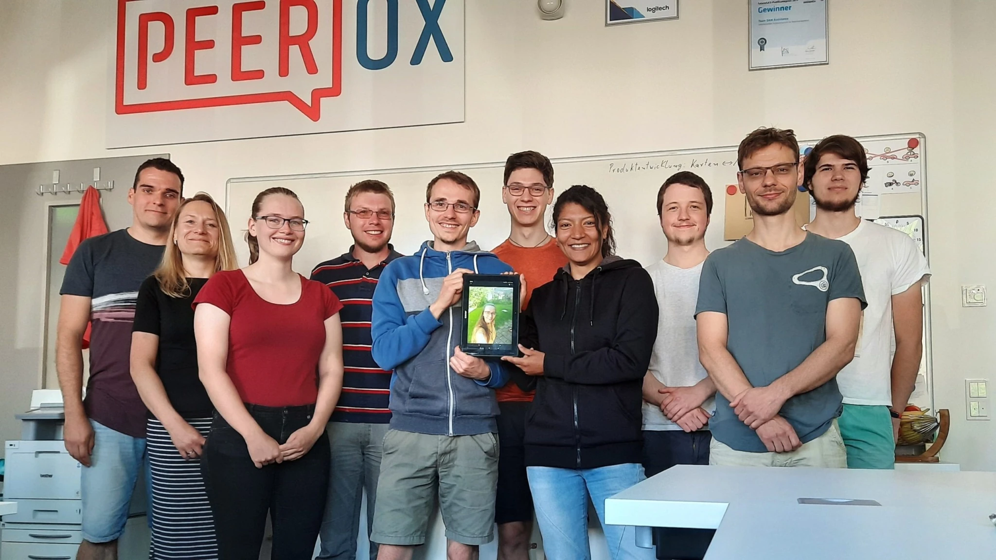Teamfoto von Peerox mit Mitarbeitenden vor einem Peerox-Logo, einer hält eine Trophäe – „Wir sind als Gründer des Jahres nominiert